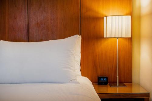 a bed with a white pillow and a table with a lamp at Orida Maidstone in Maidstone