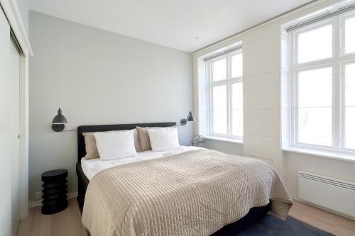 a white bedroom with a bed with white sheets and windows at 2BR in Vibrant & Colourful Nyhavn Copenhagen City in Copenhagen