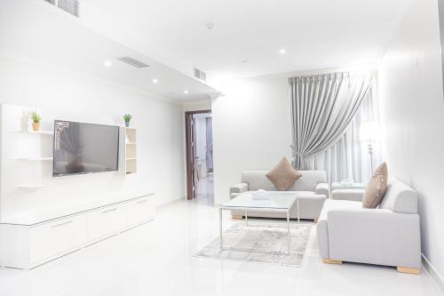 a white living room with white furniture and a tv at Mooj served Apartments موج للشقق المخدومه in Dammam