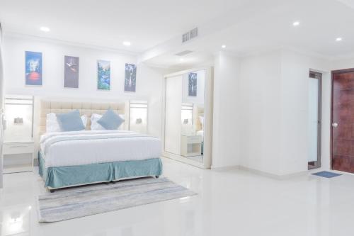 a white bedroom with a large bed with blue pillows at Mooj Apartments Hotel- فندق موج للشقق الفندقية in Dammam