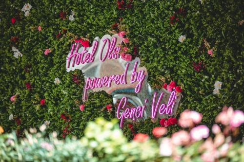 un panneau sur une haie avec des fleurs roses dans l'établissement Hotel Olsi, à Saranda