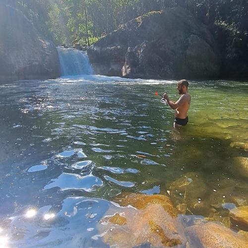 a man standing in the water near a waterfall at Pousada Vale da Cachoeira in Visconde De Maua