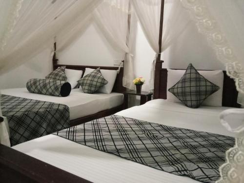 Sigiriya Rock Gate Resort في سيجيريا: سريرين بشرشف ووسائد بيضاء في الغرفة