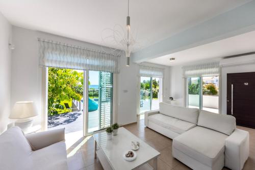 a living room with white furniture and large windows at Protaras Sunrise Zen Seafront Villa in Protaras