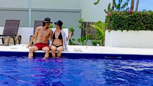 a man and woman sitting next to a swimming pool at Love Vacations Tulum in Tulum