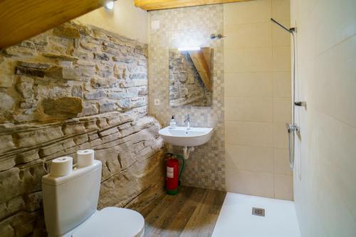 baño con lavabo, aseo y pared de piedra en Casa Barambán en Lasaosa