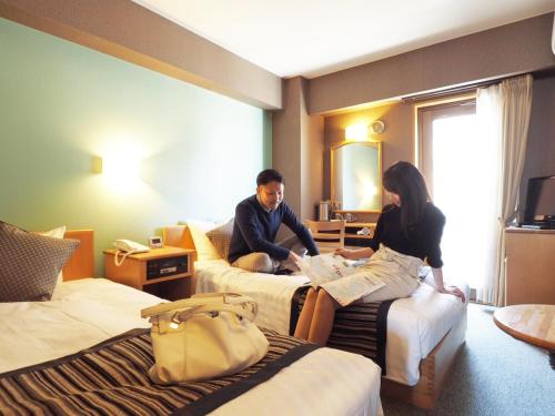 a man and a woman sitting on beds in a hotel room at Hotel AreaOne Kushiro in Kushiro