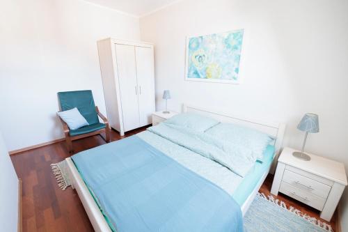 a white bedroom with a blue bed and a chair at APARTAMENTY BIAŁA MEWA in Ustka