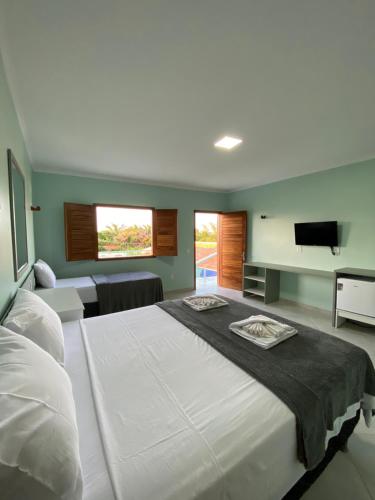 a bedroom with a large white bed and a flat screen tv at Pousada Maanain in Icapuí