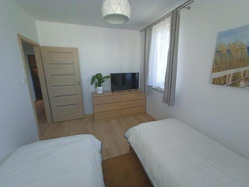 a bedroom with two beds and a tv and a window at Apartament Stogi in Gdańsk