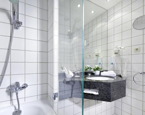 ライプツィヒにある ザハセンパルク ホテルの白いタイル張りのバスルーム(シンク、シャワー付)