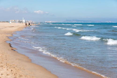 APARTAMENTO 1ª LÍNEA EN PLAYA DE GANDÍA في Playa de Gandia: شاطئ فيه ناس تمشي على الرمال والمحيط