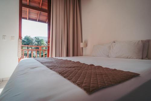 a bedroom with a white bed with a large window at Vila Bardot in Barra do Sahy