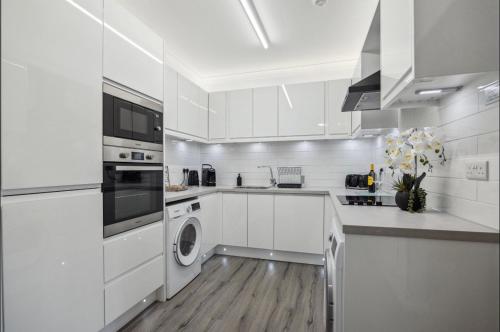 a kitchen with white cabinets and a washer and dryer at Little Gleddoch in Dumbarton