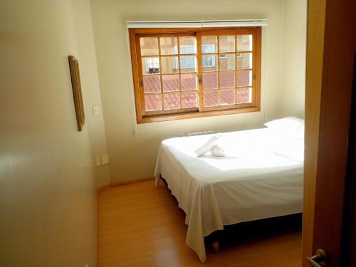um quarto com uma cama branca e uma janela em Apartamento Solar da Borges em Gramado