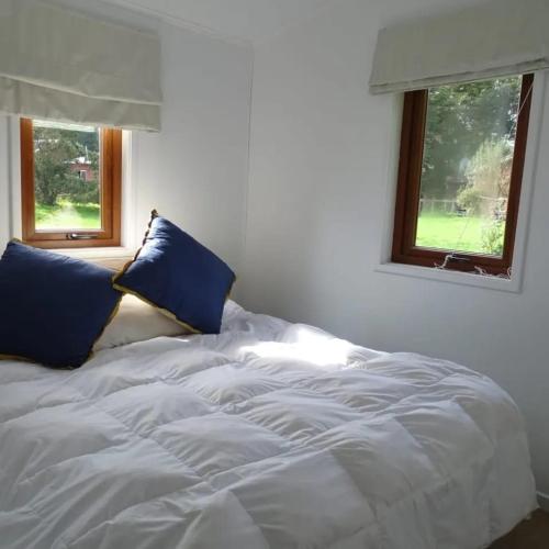 a white bed with blue pillows and two windows at CasaMisur in Puerto Varas