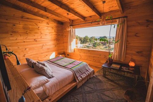 una camera da letto con un letto in una camera in legno con finestra di Casita boutique con tina exterior a Pichilemu