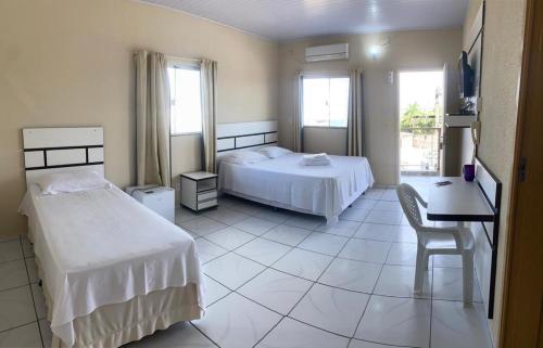 a bedroom with two beds and a table and a desk at HOTEL AVENIDA in Alta Floresta
