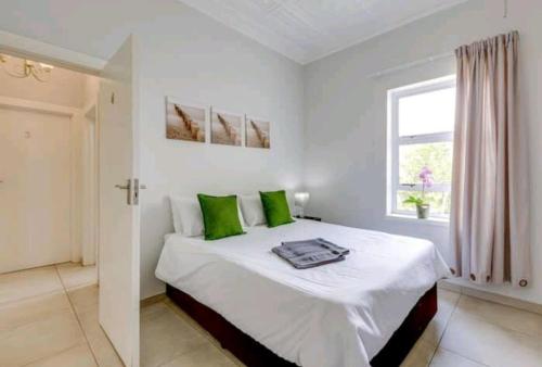 a white bedroom with a large bed with green pillows at East Prestige lodge in Johannesburg