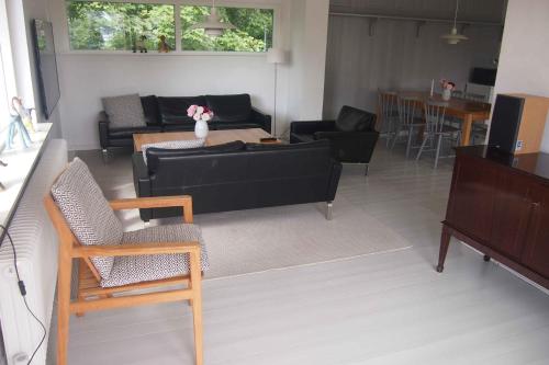 sala de estar con sofá negro y sillas en The House At The Mountain, en Lemvig