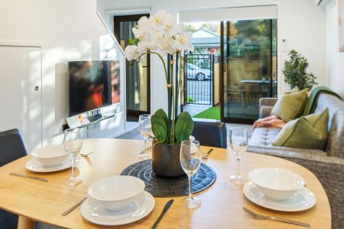 a wooden table with plates and glasses and a vase with flowers at Best of Central Christchurch 2 bed 2 bath in Christchurch