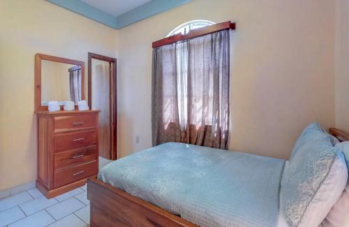 a bedroom with a bed and a dresser and a window at Sandy Feet Beach Resort in Placencia Village