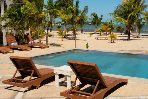 a swimming pool with chairs and a table next to a beach at Sandy Feet Beach Resort in Placencia Village