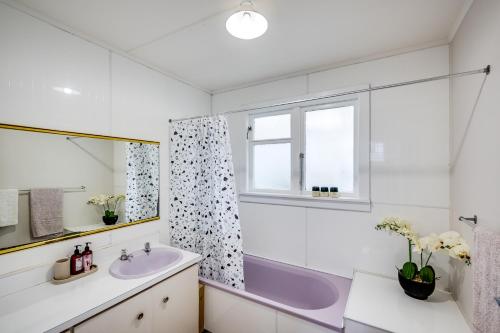 La salle de bains est pourvue d'un lavabo, d'une baignoire et d'une fenêtre. dans l'établissement Central Cottage - Napier Holiday Home, à Napier