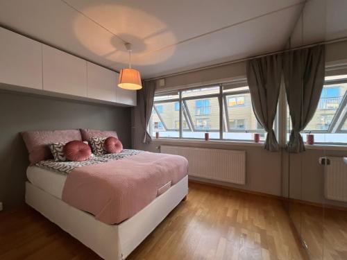 a bedroom with a bed with pink sheets and windows at City center flat w roof top terrace & free parking in Oslo