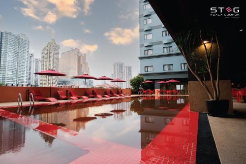 STEG Kuala Lumpur في كوالالمبور: مسبح وكراسي حمراء ومظلات على مبنى