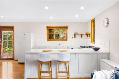 a kitchen with a white counter and two bar stools at Bunyip Cottage in Katoomba