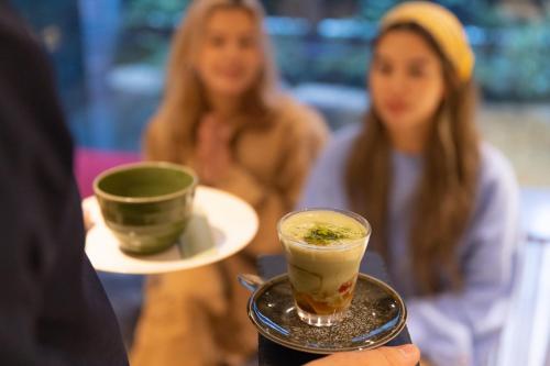 a person holding a drink on a plate with a waitress at THE BLOSSOM KYOTO in Kyoto