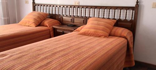 2 camas con almohadas de color naranja en una habitación de hotel en PENSION RESTAURANTE CASANOVA, en Puebla de Trives