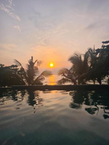 a sunset over a swimming pool with palm trees at House by the sea in Haad Tian