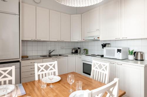 ヘルシンキにある2ndhomes Bright 2BR Apartment next to Esplanade Parkの白いキャビネット、テーブルと椅子付きのキッチンが備わります。