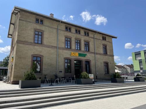 un grand bâtiment en briques avec des tables et des chaises à l'extérieur dans l'établissement Hotel-am-Bahnhof Stuttgart-Ditzingen, à Ditzingen