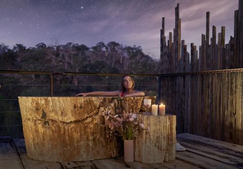 une femme assise dans une baignoire en bois avec bougies dans l'établissement Clifftop at Hepburn, à Hepburn Springs