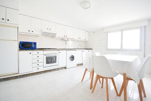 eine weiße Küche mit einem Tisch und weißen Stühlen in der Unterkunft Apartamento Vistas Vilar in Sanxenxo