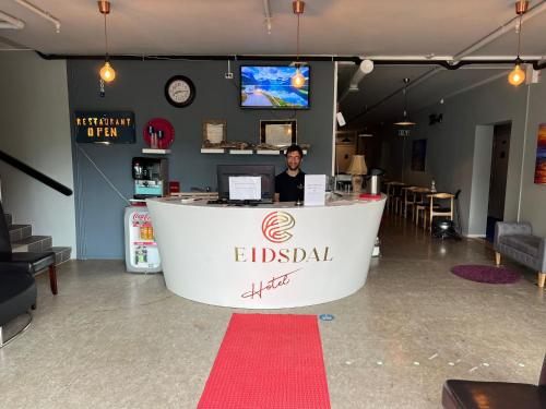 um homem sentado num balcão de recepção numa sala em Eidsdal Rest House em Eidsdal