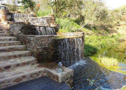 a waterfall in a stone wall next to a pond at Tala Collection Game Reserve in Silverton