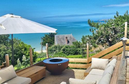 une terrasse avec un canapé et un parasol et l'océan dans l'établissement À Saint-Pair-sur-Mer - Chambre d'Hôte - Double Perspective- Manche, à Saint-Pair-sur-Mer