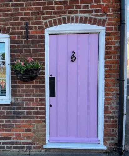 a pink door on a brick building with a potted plant at Corner Cottage with Private Parking Ten Minute Drive from Goodwood in Chichester