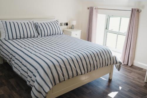 a bed with a striped comforter and a window at Tranquil Rustic Cottage in Dromore