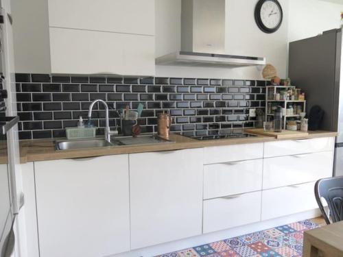 d'une cuisine avec des placards blancs et un mur en carrelage noir. dans l'établissement Apartment Fontarabie CityCosy, à Paris