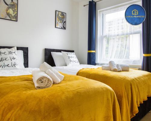 two beds with yellow sheets in a room with a window at 2 Bedroom House By Cabral Properties Monthly special price in Reading