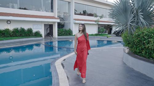 a woman in a red dress standing next to a swimming pool at Mayur Belgaum Presidency Hotel & Spa in Belgaum