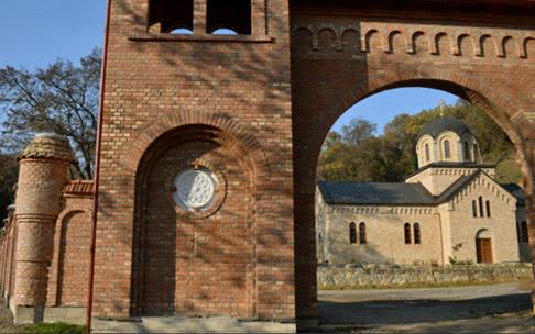 a brick building with a clock and a church at Marley kuca za odmor in Bešenovački Prnjavor