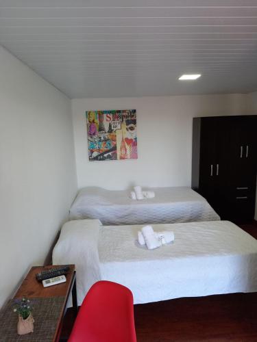 two beds in a room with a red chair and a table at Posada Don Manuel in Santa Isabel