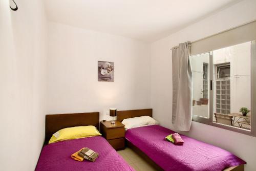 two beds in a room with purple sheets and a window at Residencial Sol Suite in Telde