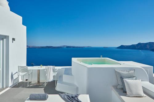a white room with a tub and a table at Katikies Santorini - The Leading Hotels Of The World in Oia